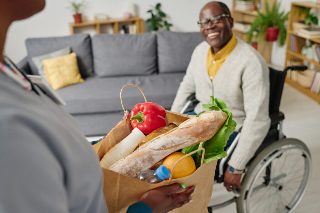 A man in a wheelchair and a caregiver in Chicago, holding a grocery bag filled with food.