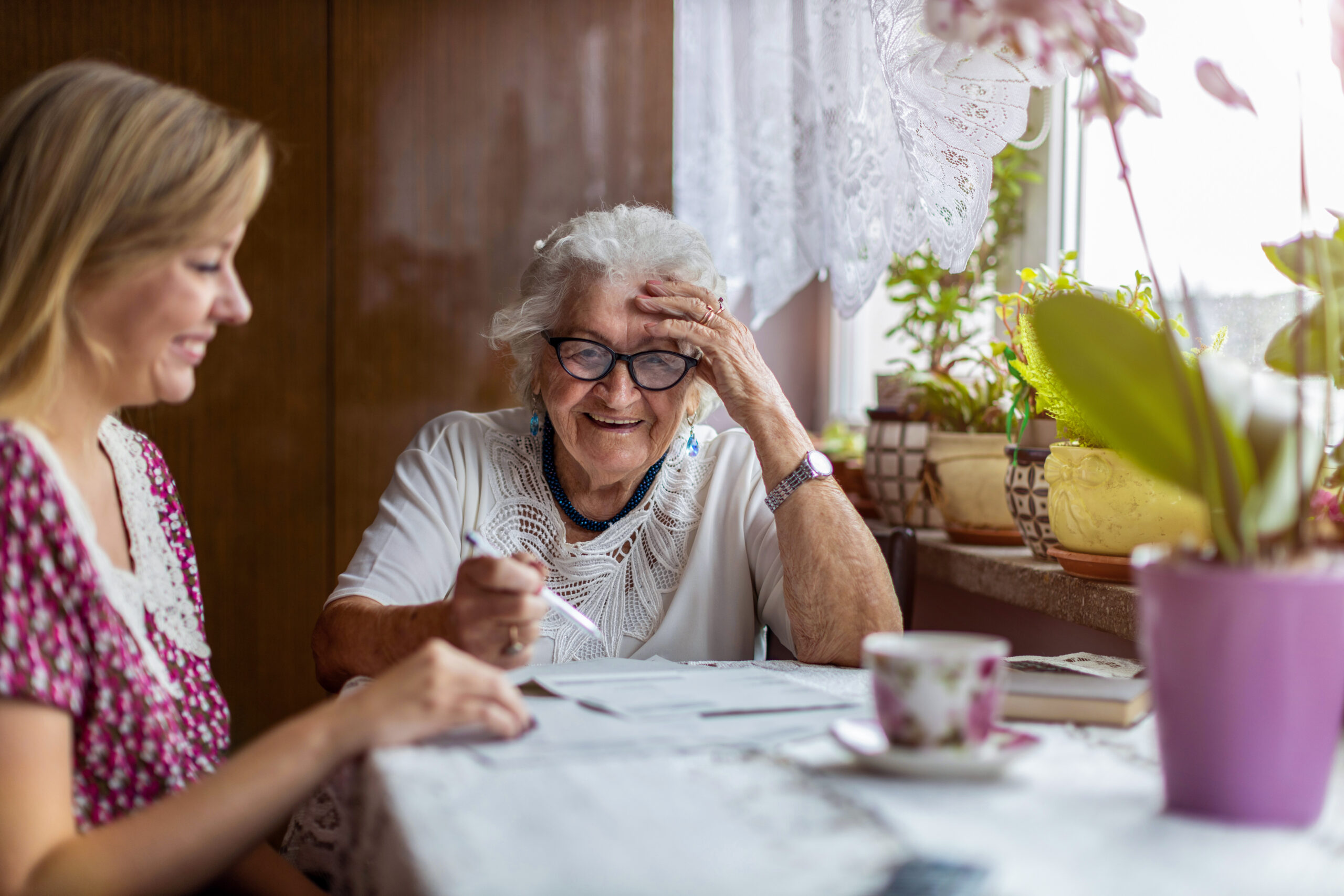 A woman and an older woman share a table, engaged in a conversation during caregiver training.