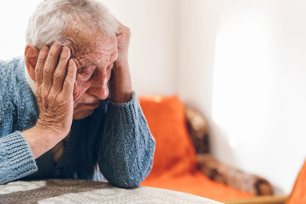 Elderly person seated at a table, looking pensive representing mental health for seniors in Chicago area.