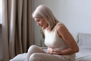 Woman sitting on the bed holding her abdomen illustrating mental symptoms of UTI in elderly