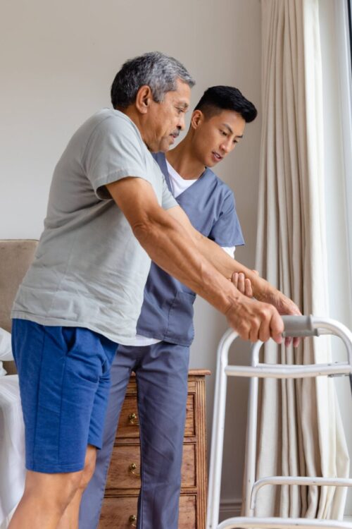 An adult being supported by a caregiver in front of a bed, symbolizing dedication in providing care in nursing homes Chicago area