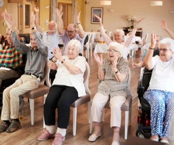 Elderly individuals, driven by strong values, sit in chairs and raise their arms in a room.